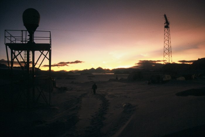 One of the winterers plodding through the deep snow around the base during the winter. There are some nacreous clouds visible in the sky.